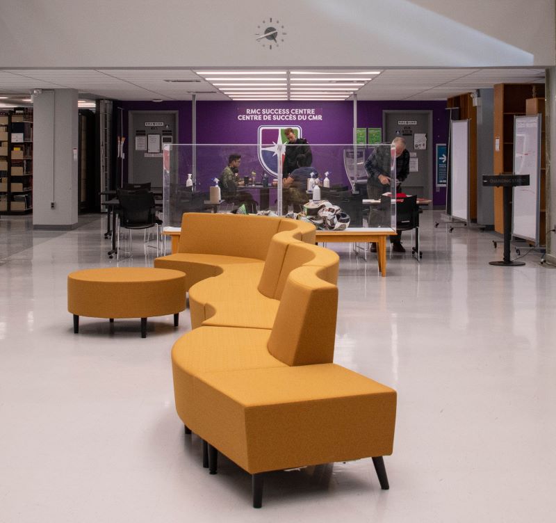 Students and staff in the lobby of the RMC Success Centre featuring a zig-zag shaped couch and a showcase on campus.